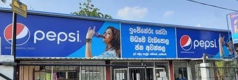 Branded dealer board above a local Indian shop promoting Pepsi, featuring bold logo, vibrant design, and local business name for high street visibility.