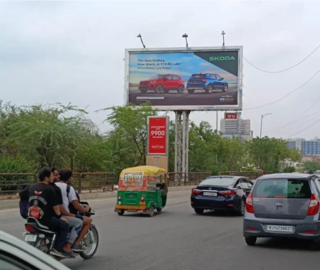 Škoda Kushaq billboard ad above a busy Indian road with cars, bikes, and an auto-rickshaw passing by, promoting the SUV's price and features.