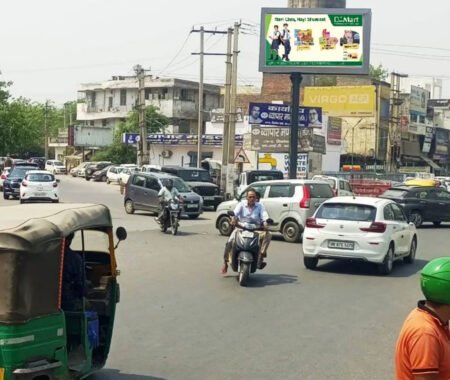 Busy Indian street intersection with a digital billboard displaying a D-Mart advertisement promoting school supplies and groceries with the tagline "Nayi Class, Nayi Shuruaat."