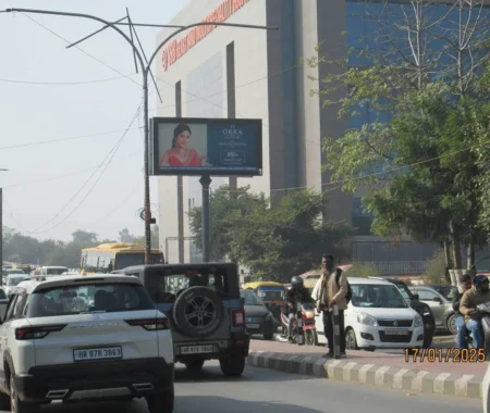 Busy city road with a digital billboard promoting ORRA Diamond Jewellery's 25% discount offer, located near a large hospitality and tourism institute building.
