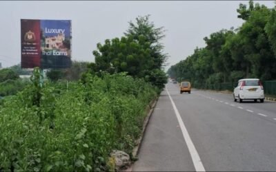 Highway hoarding in Lucknow placed on a green roadside with moving vehicles, managed by top hoarding advertising companies in Lucknow.