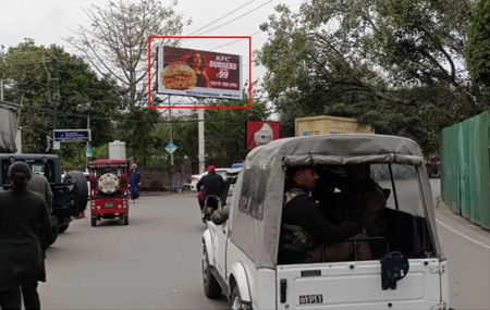 Urban street in Jammu and Kashmir with 20x10 ft KFC Digital Billboard by ACME Advertising Co., featuring burger visual and ₹99 offer; visible jeep with uniformed individuals, auto-rickshaw, truck, trees, and roadside fencing.