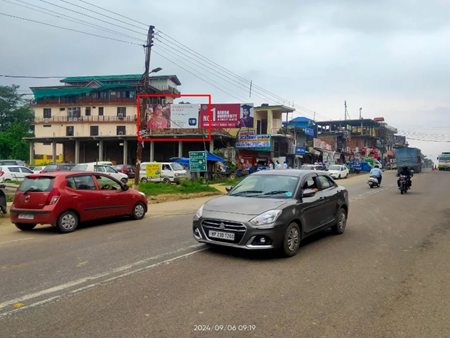 Urban street scene with 20x10 ft political hoarding by ACME Advertising Co. in Himachal Pradesh, featuring promotional visuals and logos; visible red car, motorcycles, truck, commercial buildings, and cloudy sky.