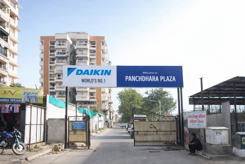 Residential plaza entrance gate with large overhead sponsor board, Indian apartment complex roadside view