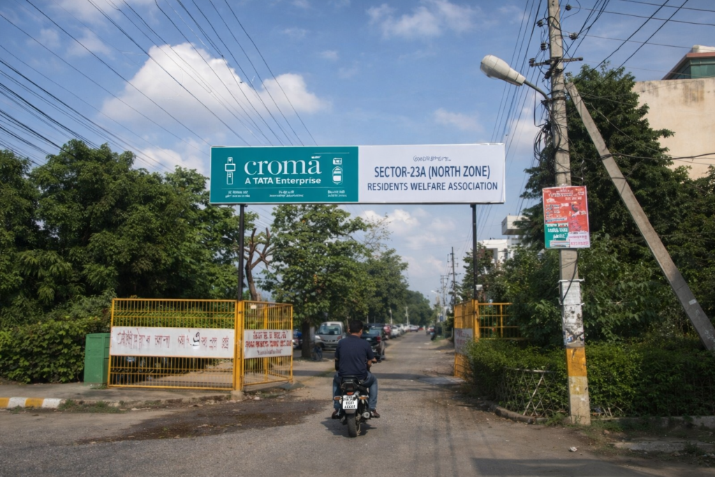 Sector entrance road in India with long overhead OOH advertising board and residential surroundings